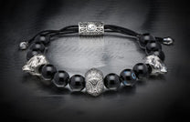 Black onyx beaded bracelet with two silver wolf heads, a central carved silver bead, an adjustable cord, and one blue eye bead.