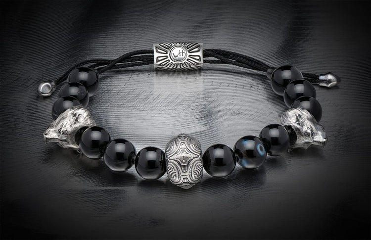 Black onyx beaded bracelet with two silver wolf heads, a central carved silver bead, an adjustable cord, and one blue eye bead.