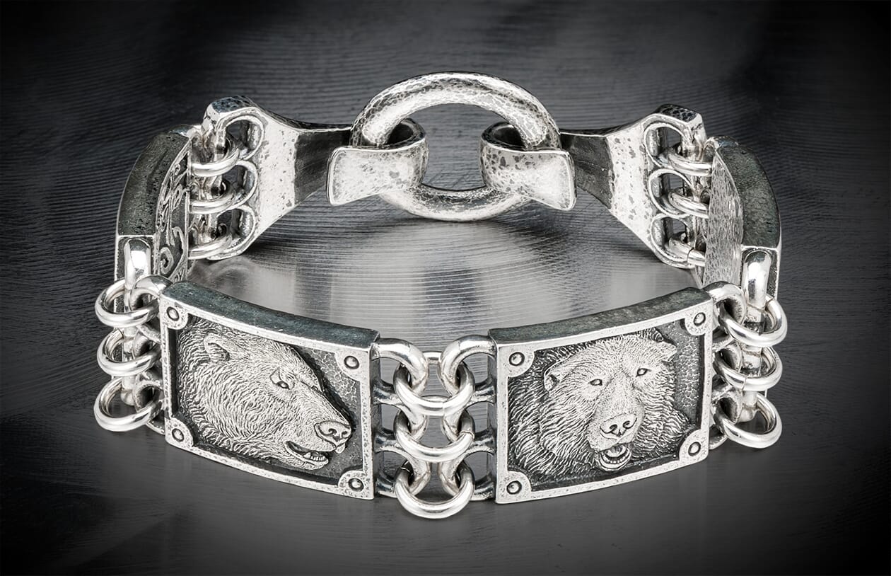 Silver metal bracelet featuring two detailed bear head engravings and an ornate chain link design.