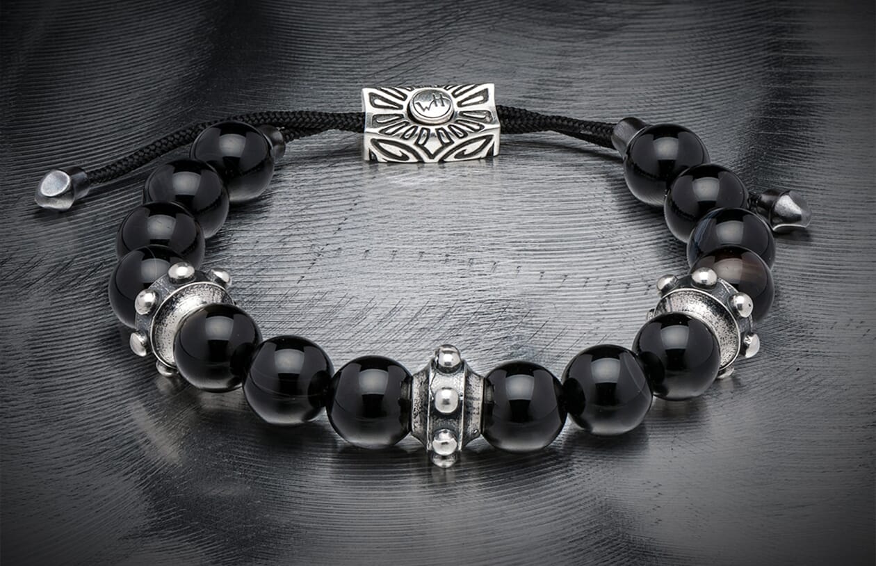 Black sardonyx bead bracelet with silver decorative spacers, a slider charm featuring 'WH' logo, and black braided cord.
