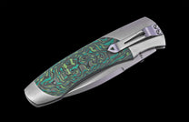 Grey folding knife with a green and dark grey swirling patterned handle scale and pocket clip.