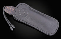 Dark Damascus steel knife with dark leather sheath by B05, featuring embossed logo and braided cord, side view on black background
