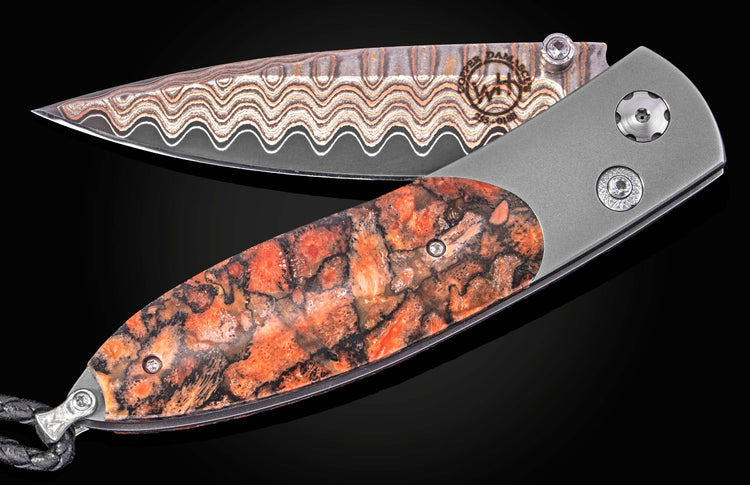 Coral-patterned folding knife with damascus steel blade by B05 Ignis, featuring textured orange and black handle, silver hardware, and braided lanyard, shown open on black background.