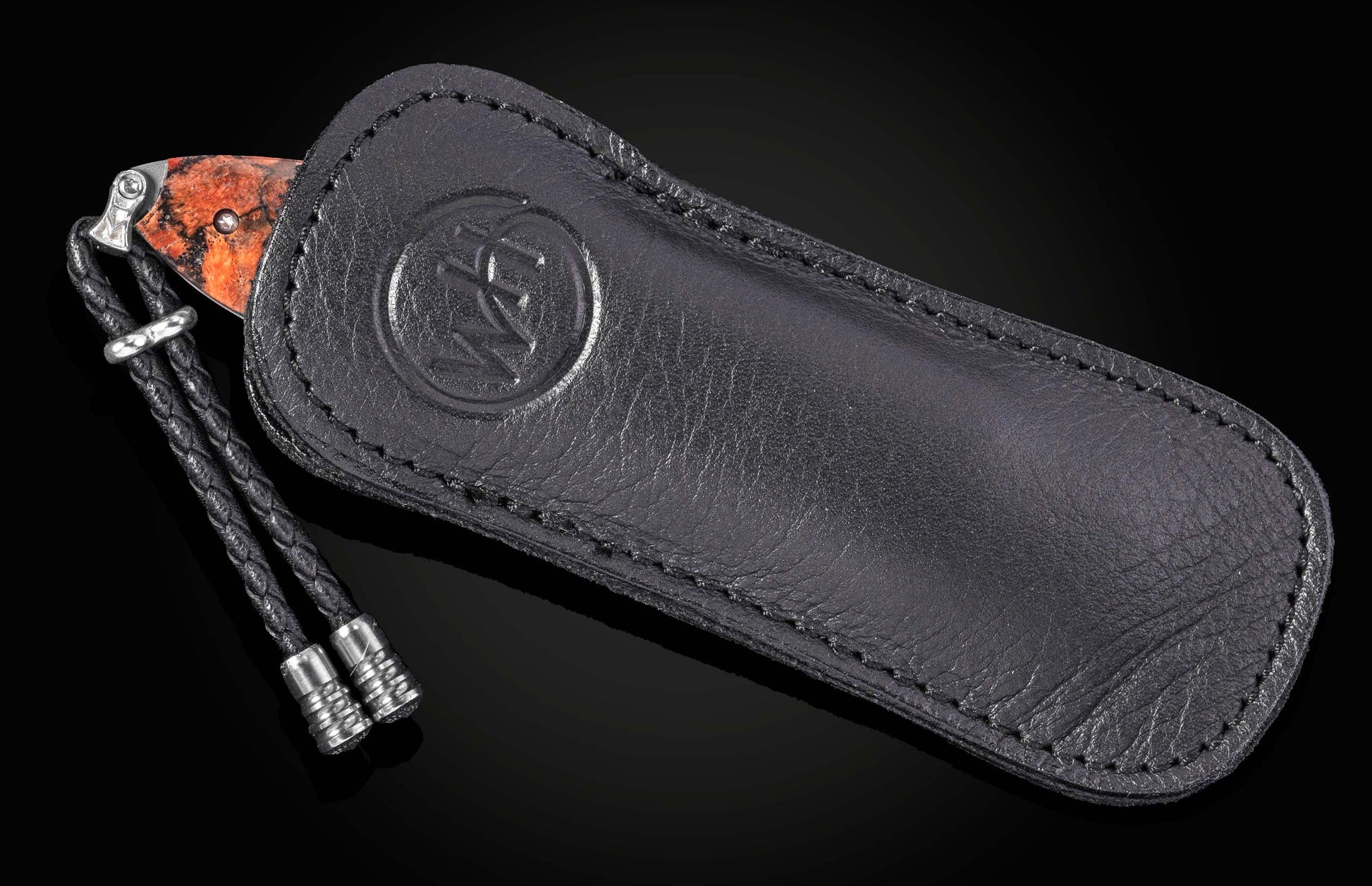 Coral-handled folding knife by B05 Ignis, partially sheathed in black leather with embossed logo and braided cord, side view.