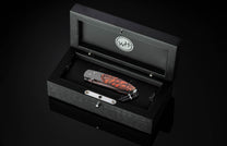 Coral-patterned folding knife with textured handle by B05 Ignis, displayed in sleek black presentation box with silver hardware, top-down view.