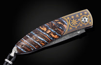 Ornate folded knife with a blue and brown fossilized handle, featuring gold star engravings, a Damascus steel blade, and a leather lanyard.