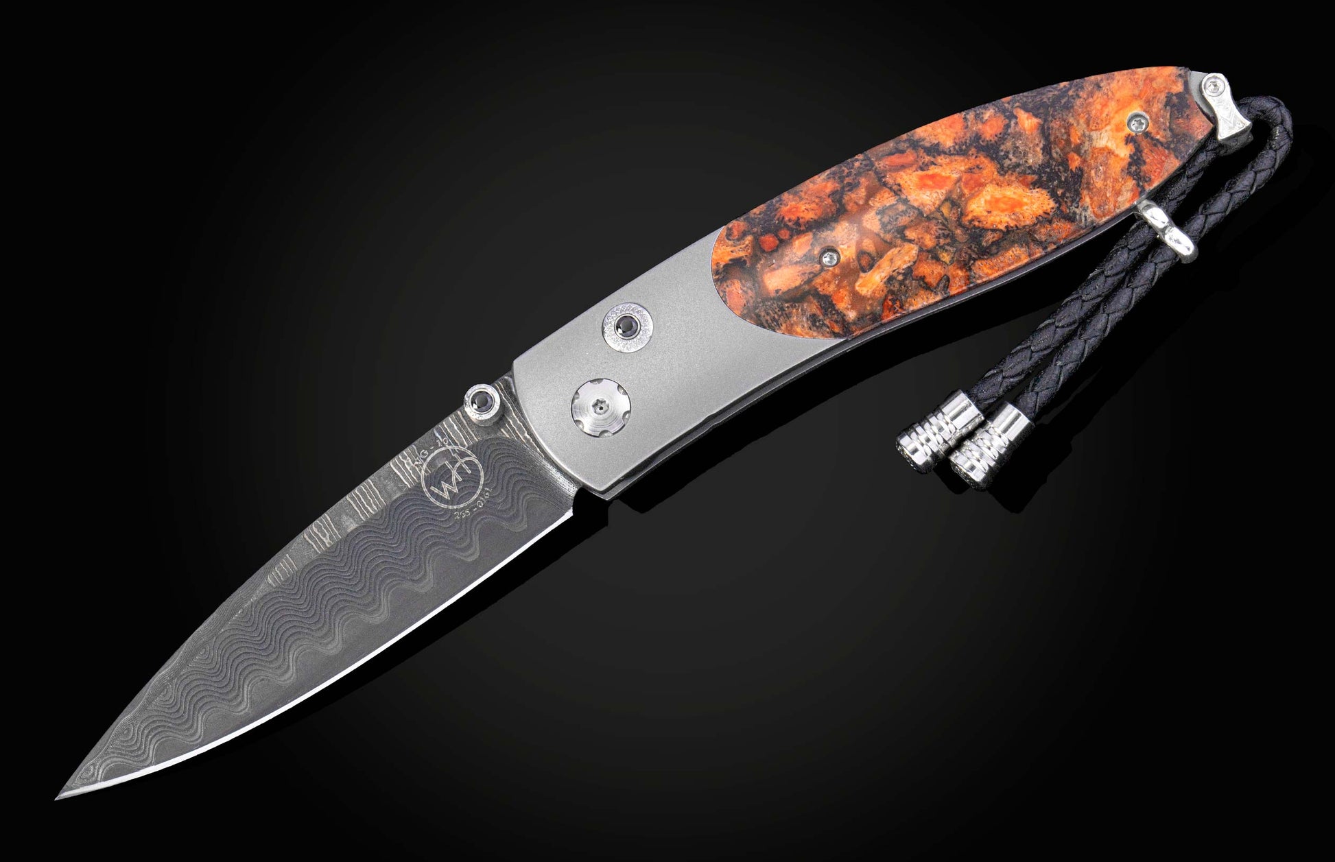 A folding knife with a wavy-patterned silver blade, marbled orange and black handle, and a braided black leather lanyard.