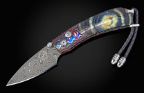 Folding knife with patterned Damascus steel blade and iridescent handle featuring blue, green, and orange swirls, with a dark braided lanyard.