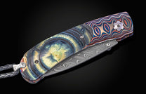 Folding knife with iridescent blue, green, and yellow 'glacial eye' handle, colorful wavy scales, Damascus steel frame, and braided lanyard.