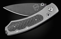 Dark gray folding knife with a wavy pattern blade and metallic gray handle with textured carbon fiber inserts.