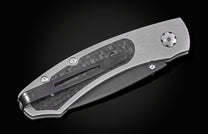 Silver-gray folding knife with carbon fiber inlay and dark pocket clip against a black background.