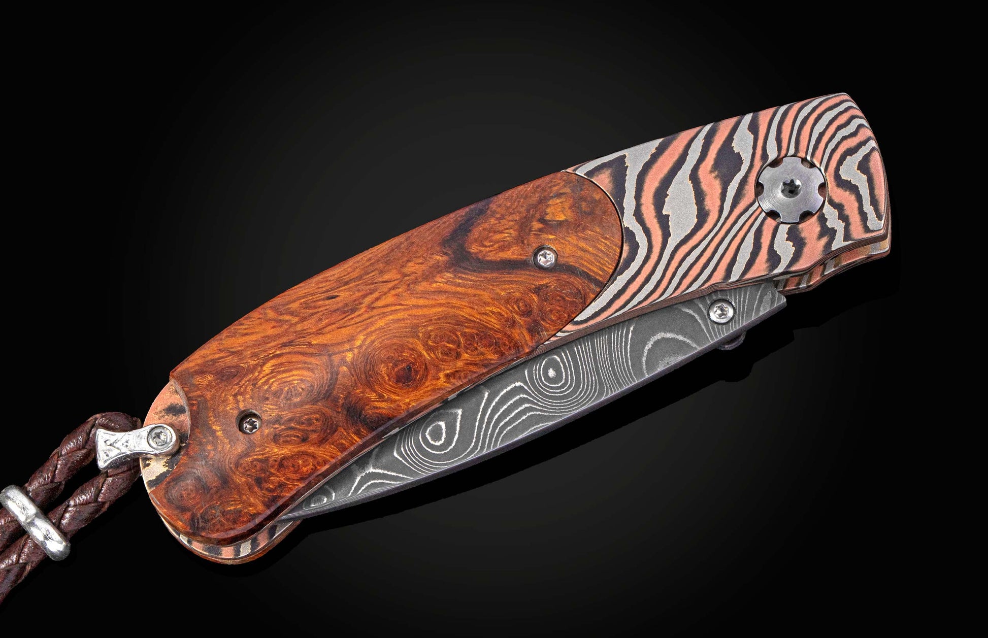 Folding knife with burl wood handle and copper and silver damascus scales, featuring a damascus blade and a braided leather lanyard.
