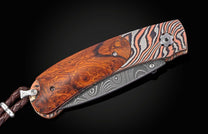 Folding knife with burl wood handle and copper and silver damascus scales, featuring a damascus blade and a braided leather lanyard.