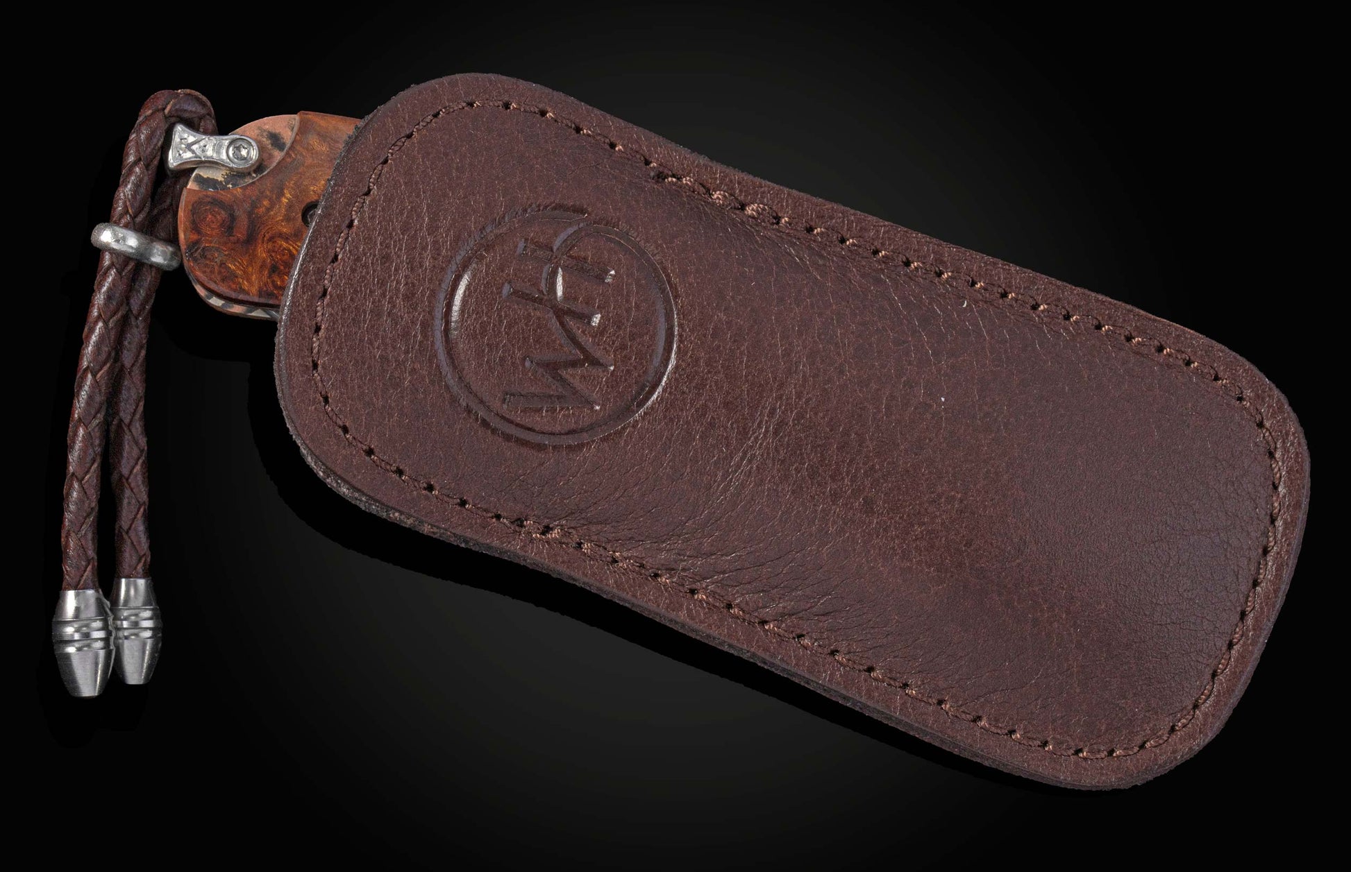 Brown leather knife sheath with a debossed logo and stitching, partially revealing a wooden-handled knife and braided lanyard.