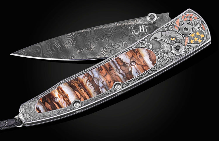 Damascus steel folding knife by B10 with engraved eagle head, amber inlay, and ornate silver handle, side view on black background