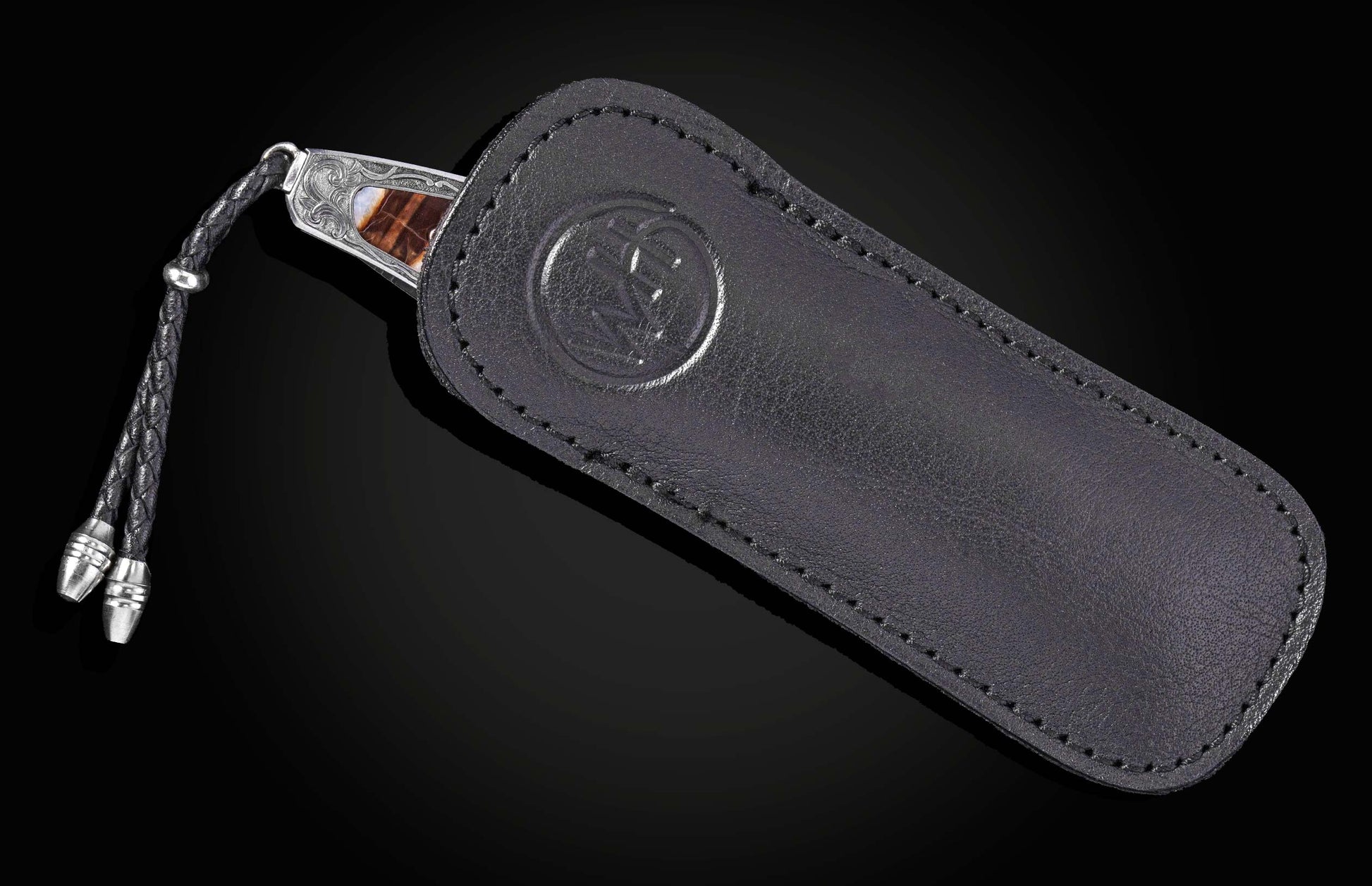 Stainless steel folding knife with amber inlay and braided lanyard, by American Eagle, in black leather sheath with embossed logo, side view