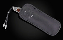 Stainless steel folding knife with amber inlay and braided lanyard, by American Eagle, in black leather sheath with embossed logo, side view