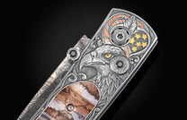 Silver folding knife with detailed eagle engraving and amber inlay, by B10, featuring stars, feathers, and textured metalwork, side view.