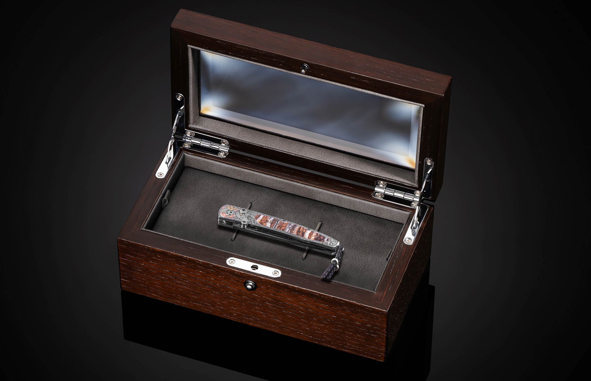 Stainless steel folding knife with marbled brown handle by American Eagle, displayed in dark wood presentation box with glass lid, top-down view