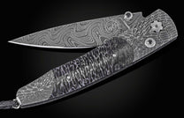 Damascus steel folding knife with wavy pattern and textured handle, by B10 Mammuthus, featuring engraved logo and dark lanyard, side view on black background