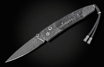 Damascus steel folding knife with wave pattern and braided lanyard, by B10, side view on black background