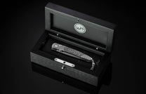 Stainless steel folding knife with damascus pattern handle by W.H. in black wooden box, top-down view