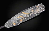 Silver folding knife with engraved Statue of Liberty and fireworks, by B12, featuring gold accents and eagle detail, side view on black background