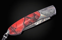Folding knife with a red cracked handle, engraved Damascus steel blade depicting a classic car on a road, and a black leather lanyard.