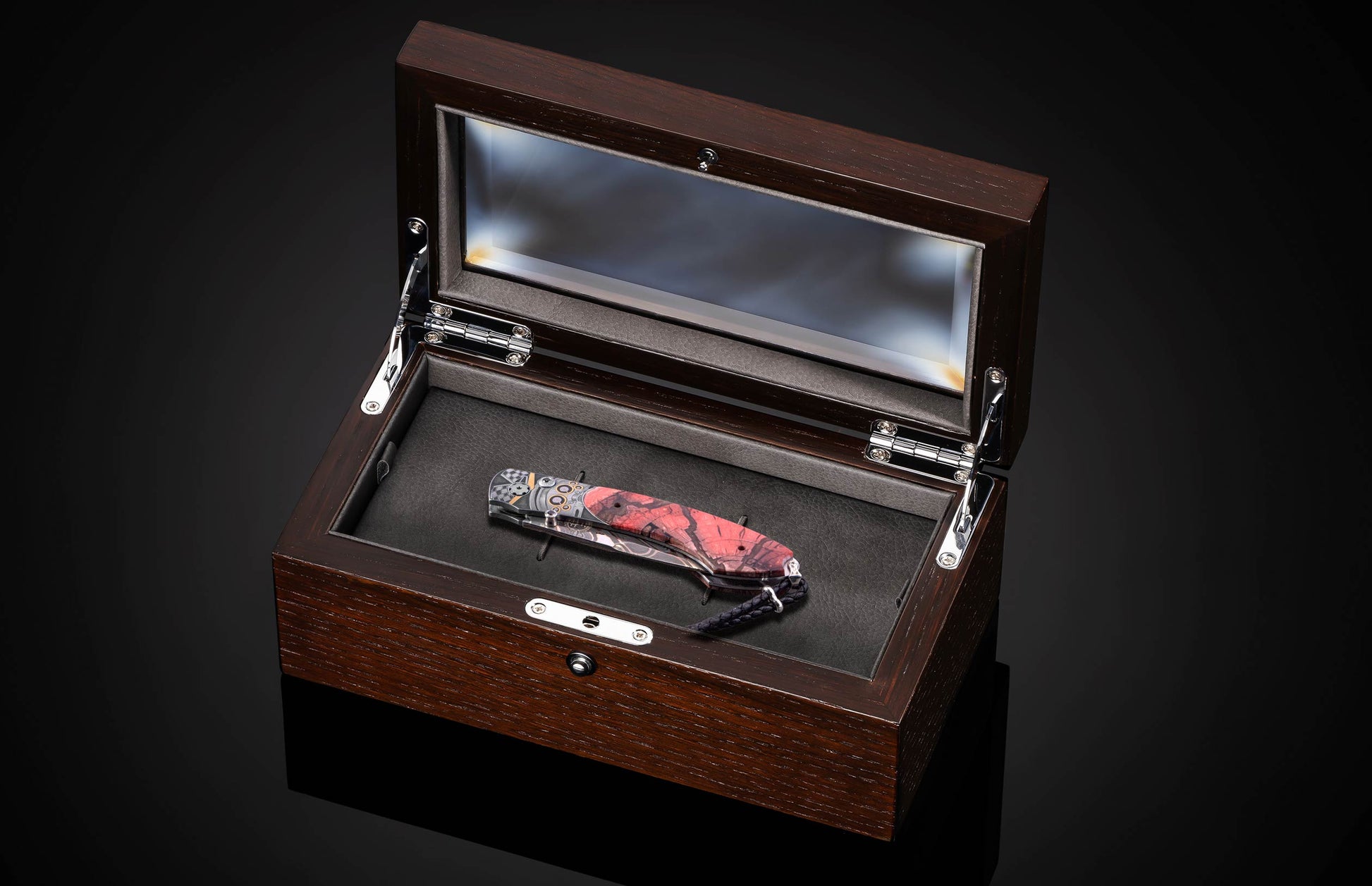 Folding knife with red and black marbled handle and metallic engine-like details, inside an open dark brown wooden display box.