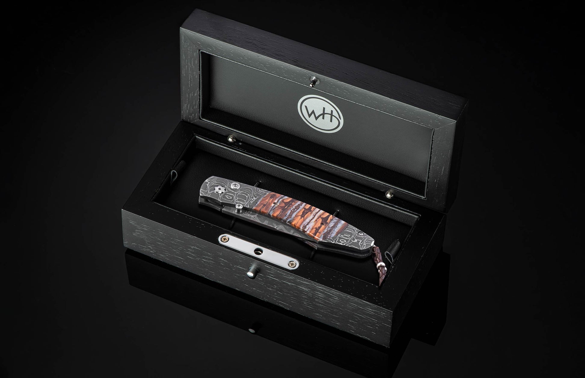 Folding knife with Damascus patterned blade and auburn and grey striped handle, in an open black wooden presentation box with a WH logo.