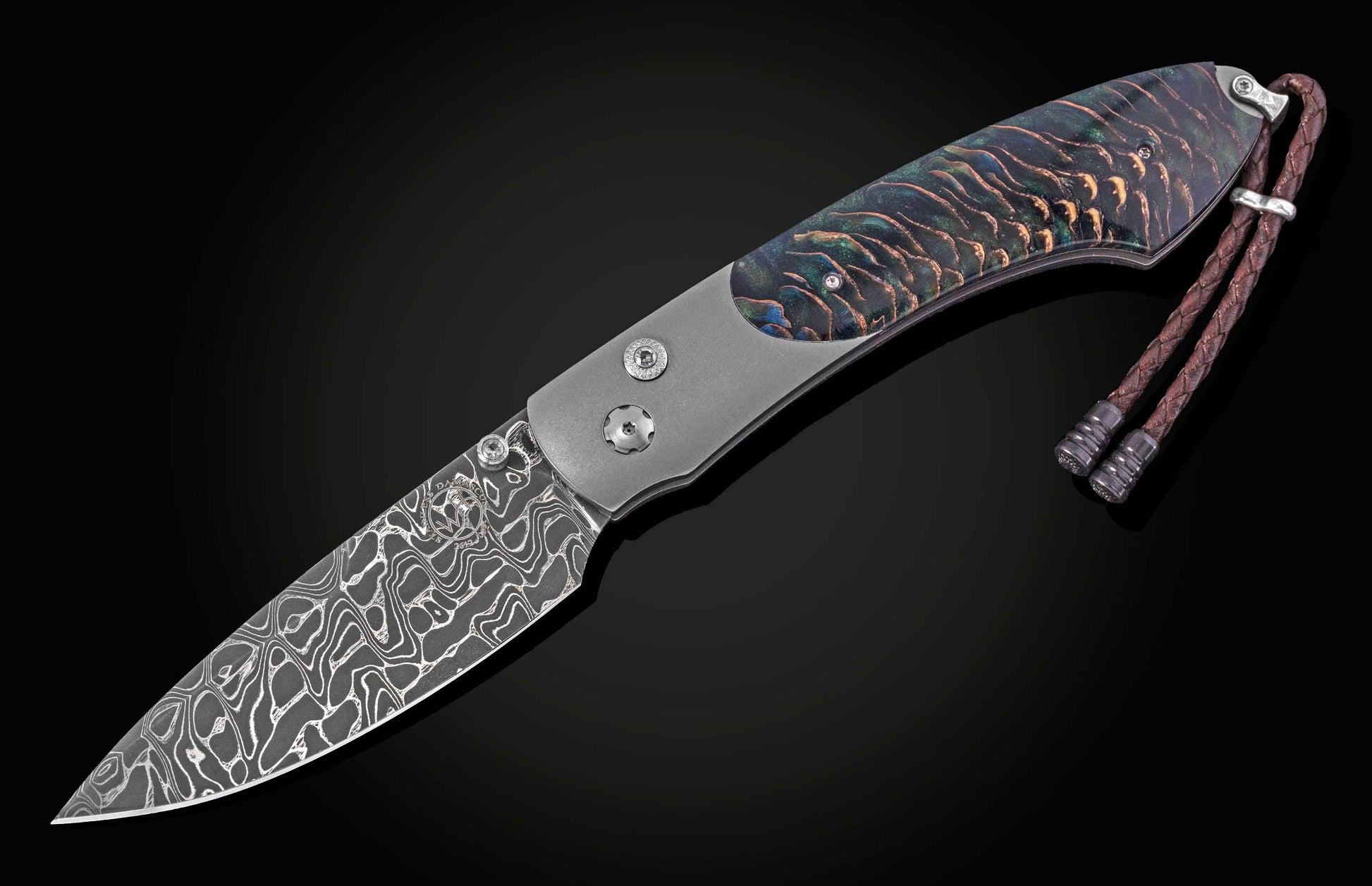 Damascus steel knife with iridescent pine resin handle by B12, featuring braided leather lanyard and textured silver hardware, side view on black background