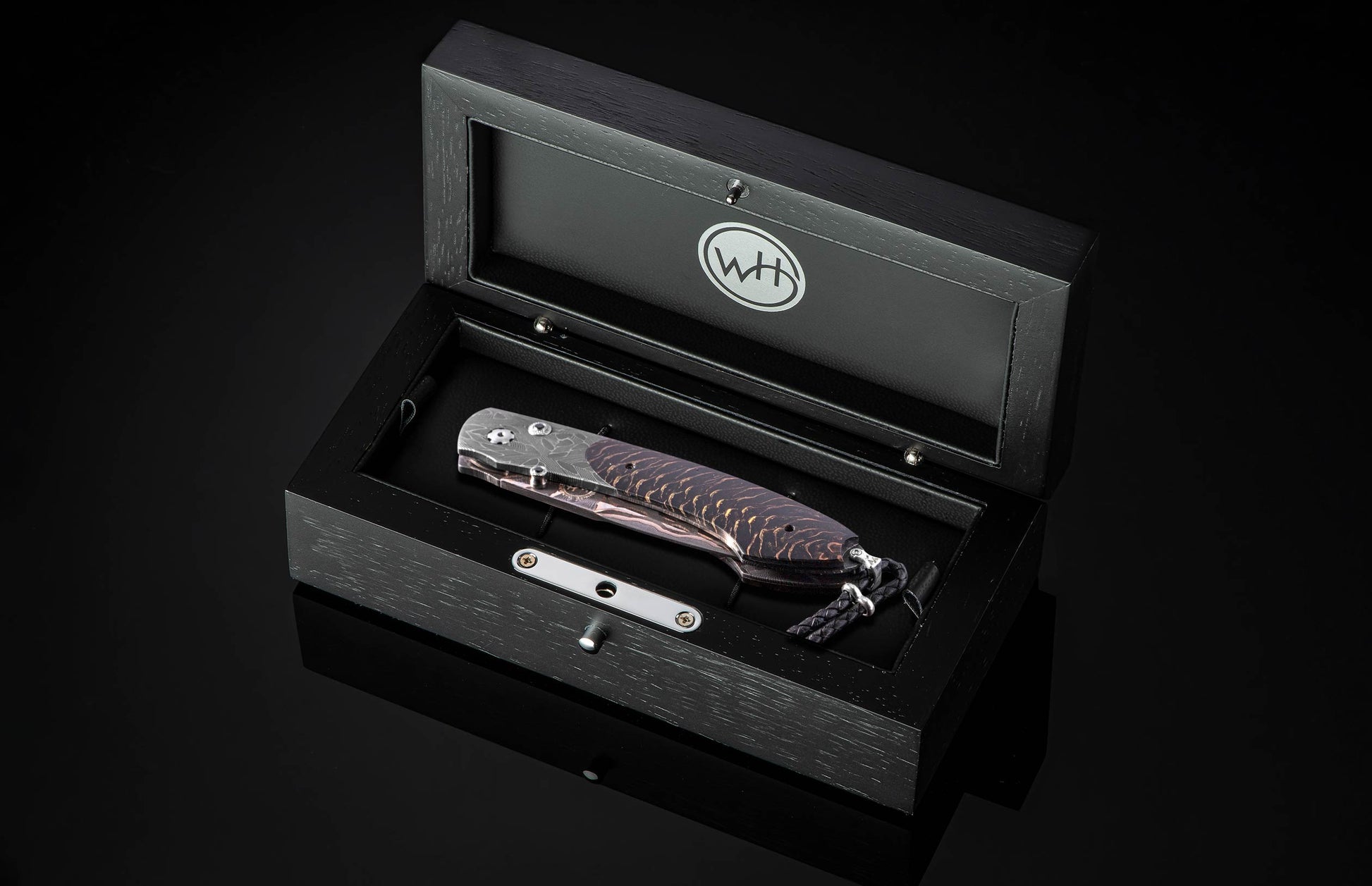 Black folding knife with dark wood grain handle and Damascus steel blade, by B12, displayed in luxury black presentation box with silver accents