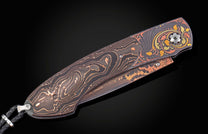 Dark Damascus folding knife with intricate copper-toned patterns, gold and orange leaf engravings, and a black leather lanyard.