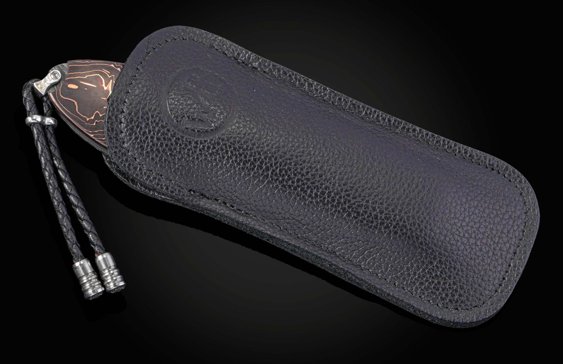 Folding knife with a dark blade and copper-colored wavy pattern, partially sheathed in a black pebbled leather case with a braided lanyard.