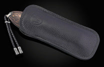 Folding knife with a dark blade and copper-colored wavy pattern, partially sheathed in a black pebbled leather case with a braided lanyard.