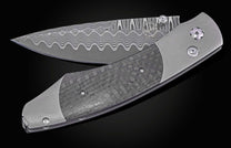 Folding knife with a dark, textured carbon fiber handle, grey titanium frame, and wavy patterned Damascus blade, partially open on a black background.