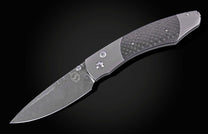 Titanium folding knife with dark carbon fiber inlay and a patterned Damascus steel blade.
