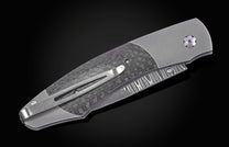 Closed folding knife with grey handle, carbon fiber inlay, wavy patterned blade, and pocket clip.