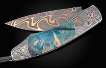 Open artisan folding knife with swirling Damascus blade, blue and teal wood handle, and engraved silver bolsters with colored accents.