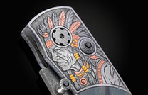 Ornate knife featuring a detailed engraving of a Native American chief with a feather headdress, accented in silver, copper, and gold, with black gemstones.