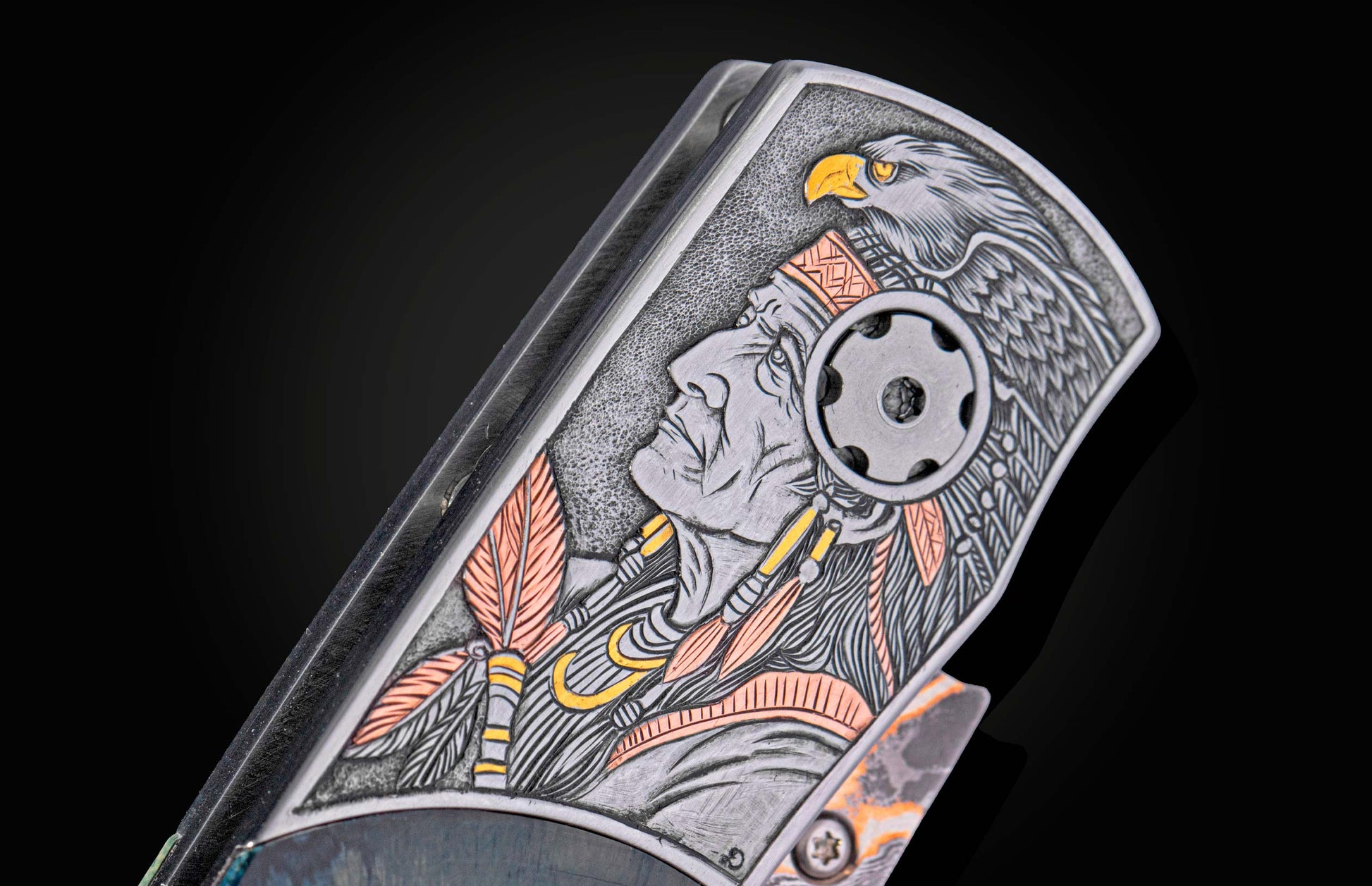 Knife handle with intricate metallic engraving of a Native American chief profile and eagle, featuring silver, copper, and yellow accents.