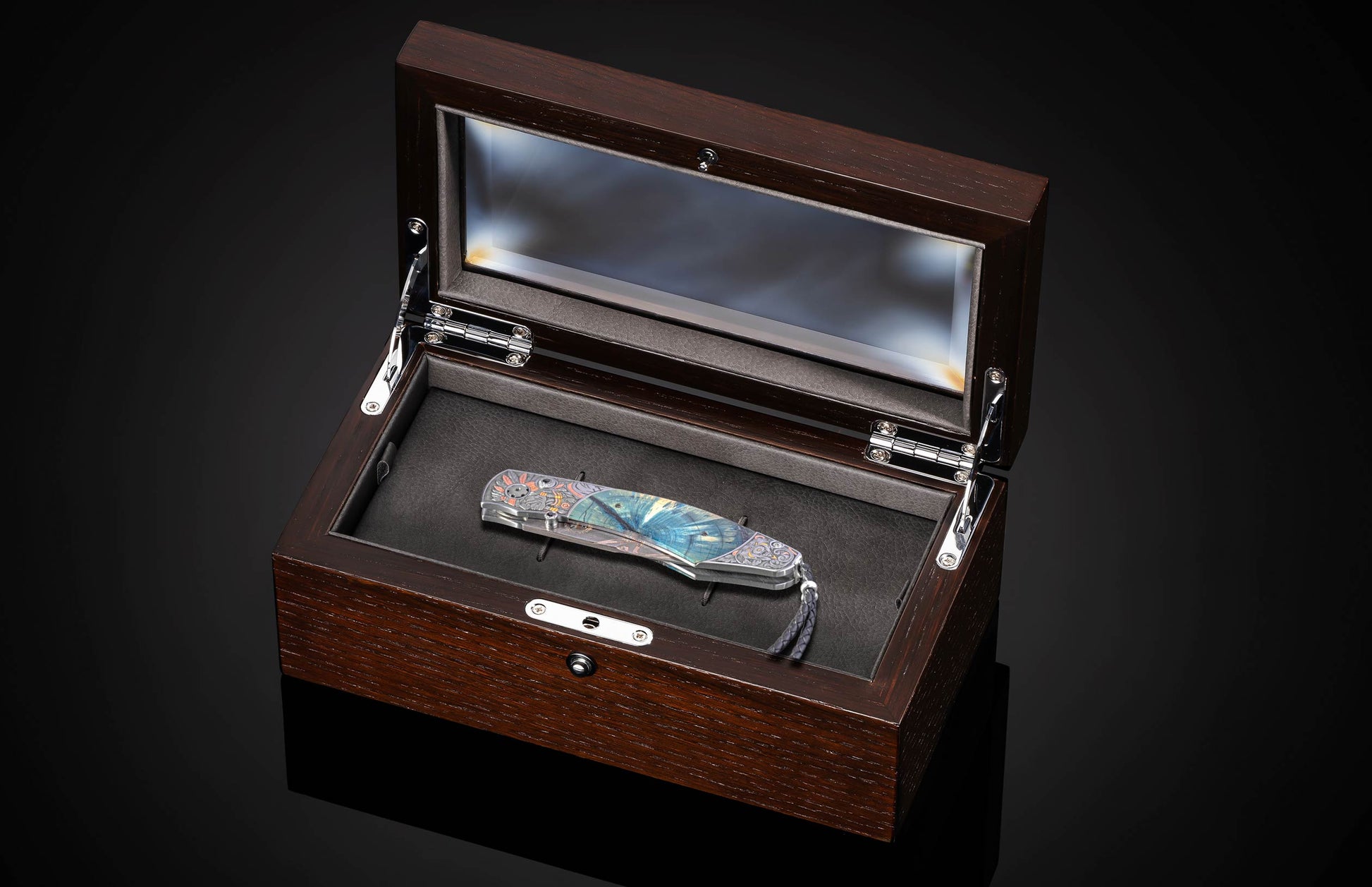 Ornate folding knife with a vibrant blue and multicolored decorative handle and lanyard, presented in an open wooden display box.