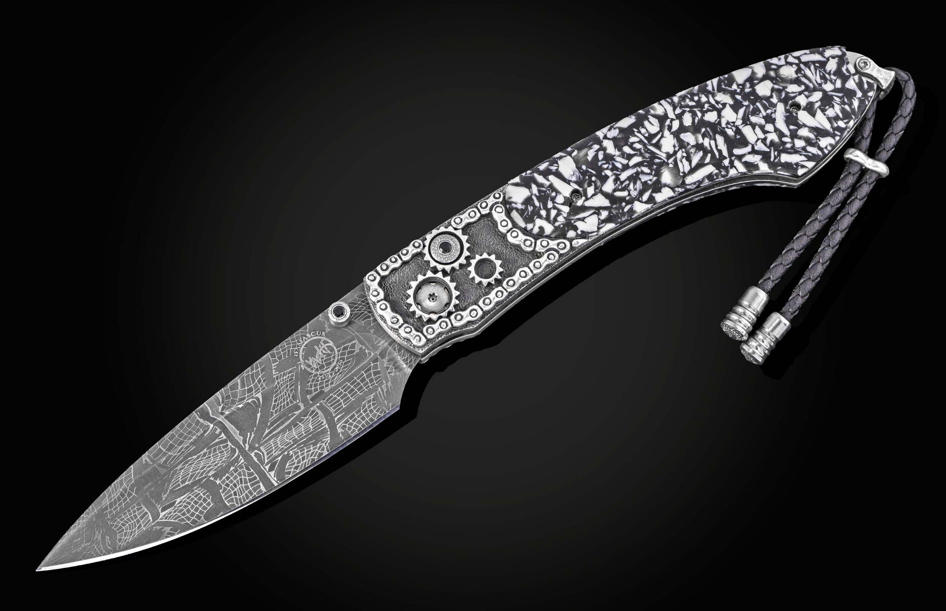 Damascus steel folding knife with black and white mosaic handle by B12, featuring gear embellishments and braided lanyard, side view on dark background