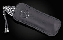 Luxury Damascus steel knife with black leather sheath by B12, featuring embossed logo and braided cord accent, side view on dark background