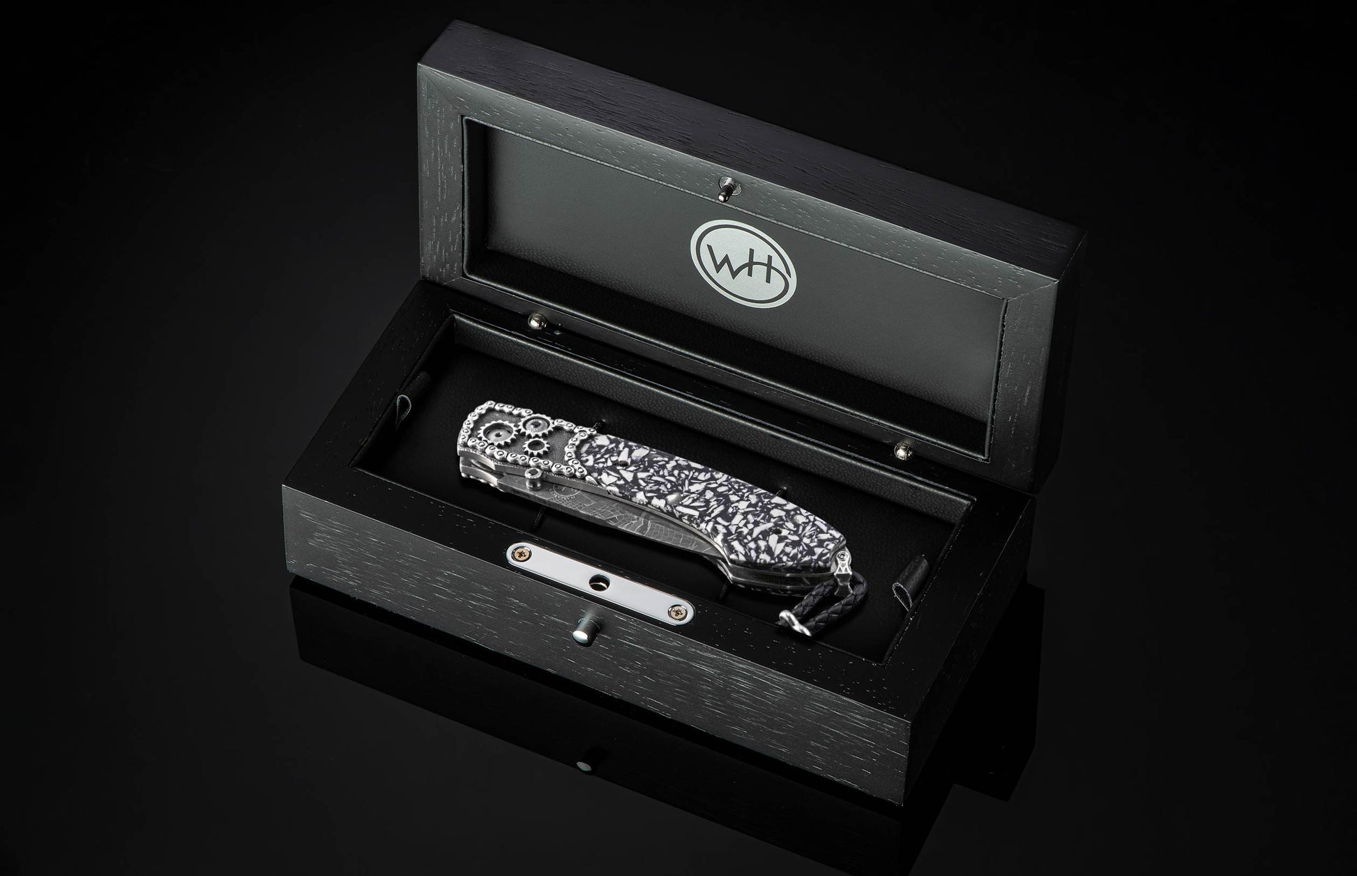 Luxury folding knife with black and white marbled handle and gear detailing, by B12, displayed in sleek black presentation box.