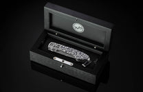 Luxury folding knife with black and white marbled handle and gear detailing, by B12, displayed in sleek black presentation box.