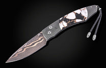 Damascus steel knife with white and black stone inlay handle by B12, featuring braided cord lanyard and wave-pattern blade, side view on black background