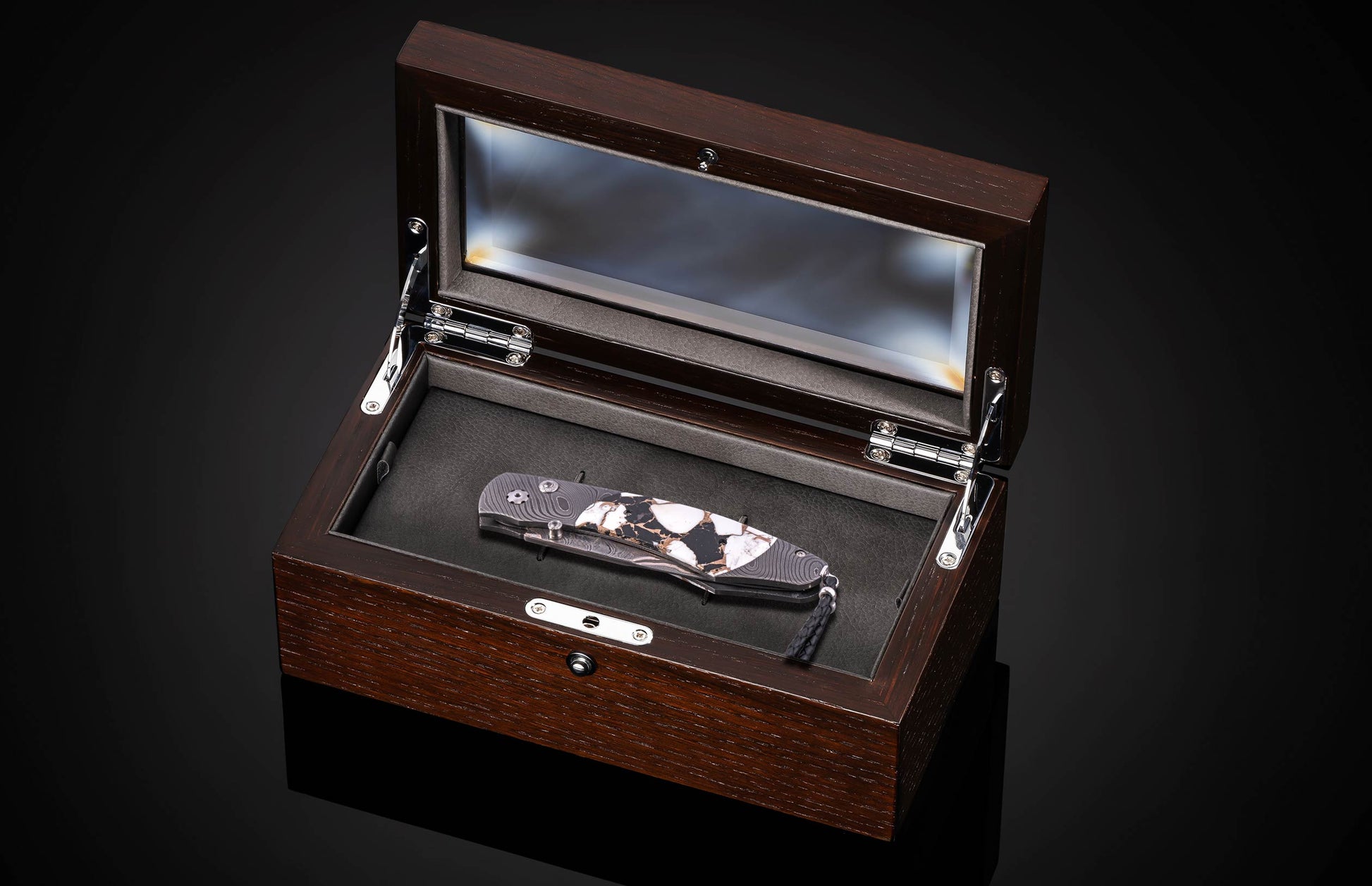 Luxury folding knife with black and white marbled handle, by B12, displayed in polished wood presentation box with glass lid, top-down view