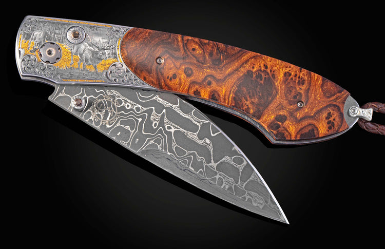 Ornate folding knife with a burl wood handle and Damascus blade, featuring silver engraving with gold elk motifs and a braided leather lanyard.