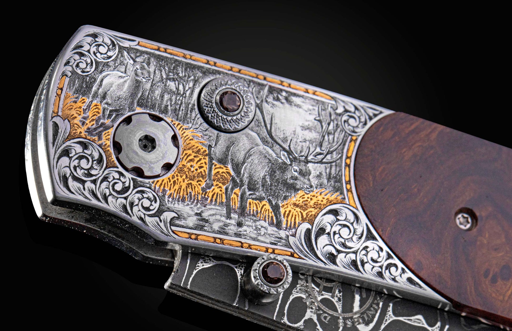 Engraved metallic knife with an elk hunting scene, gold accents, brown wood handle, and decorative gem-set fasteners.